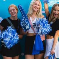 students posing in front of CAB backdrop at Laker Kickoff photo booth and holding pom poms